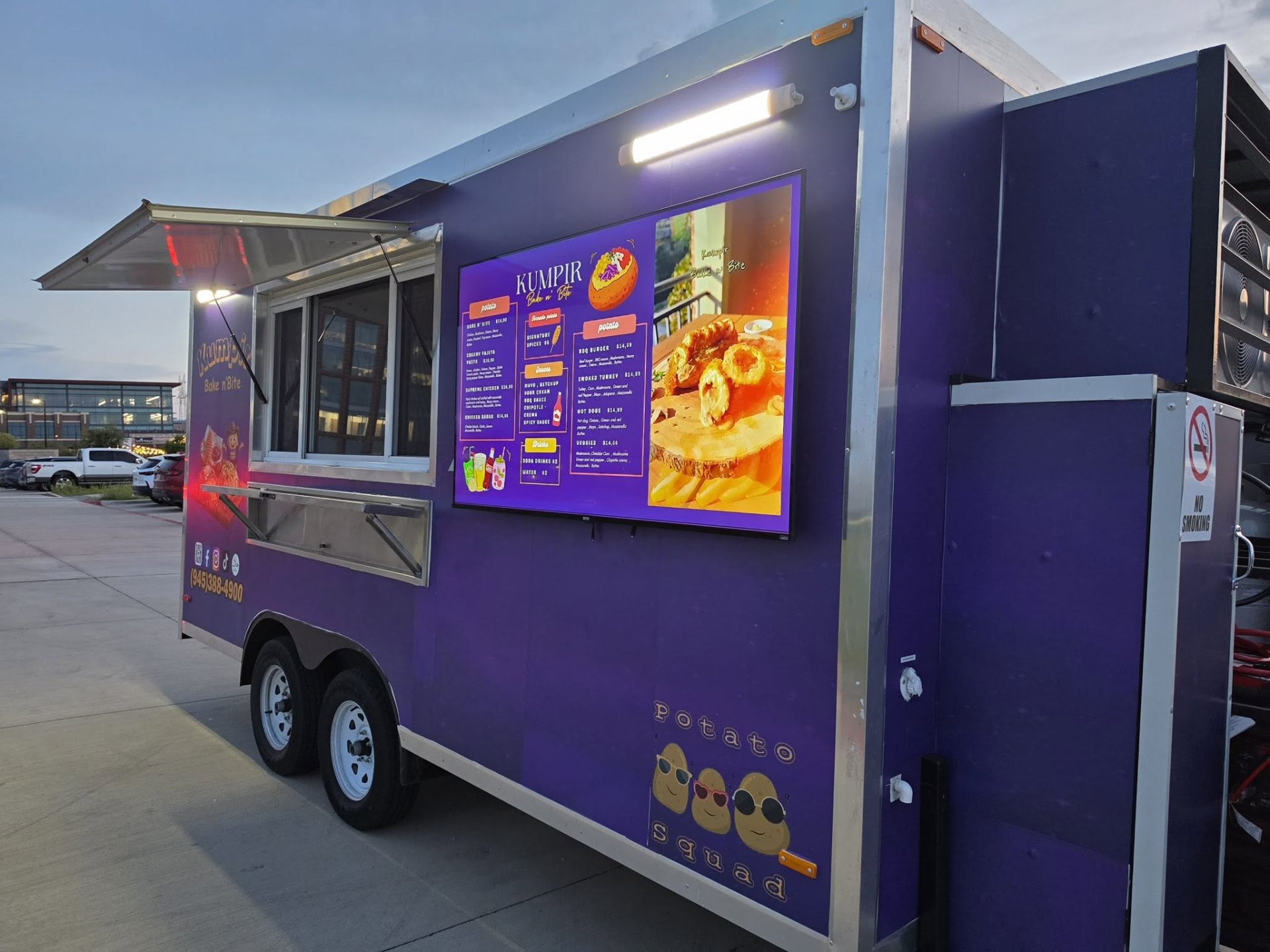 Kumpir Bake n' Bite trailer serving window with menu board at dusk